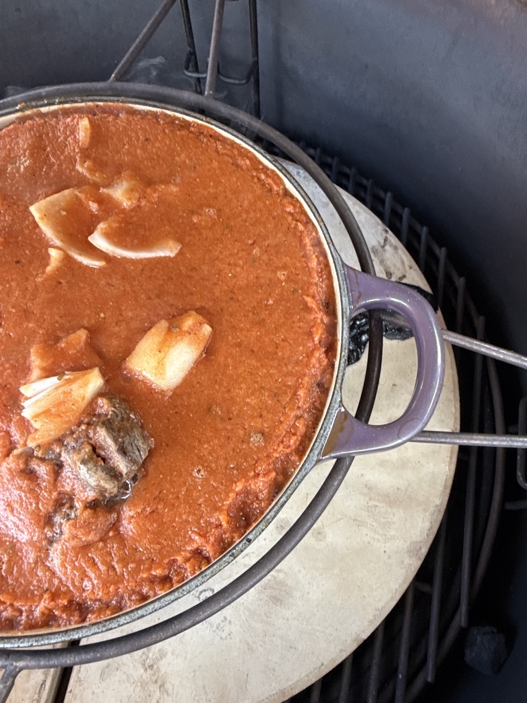Close view of birria sauce and beef cooking in a cast iron pot inside a Kamado BBQ