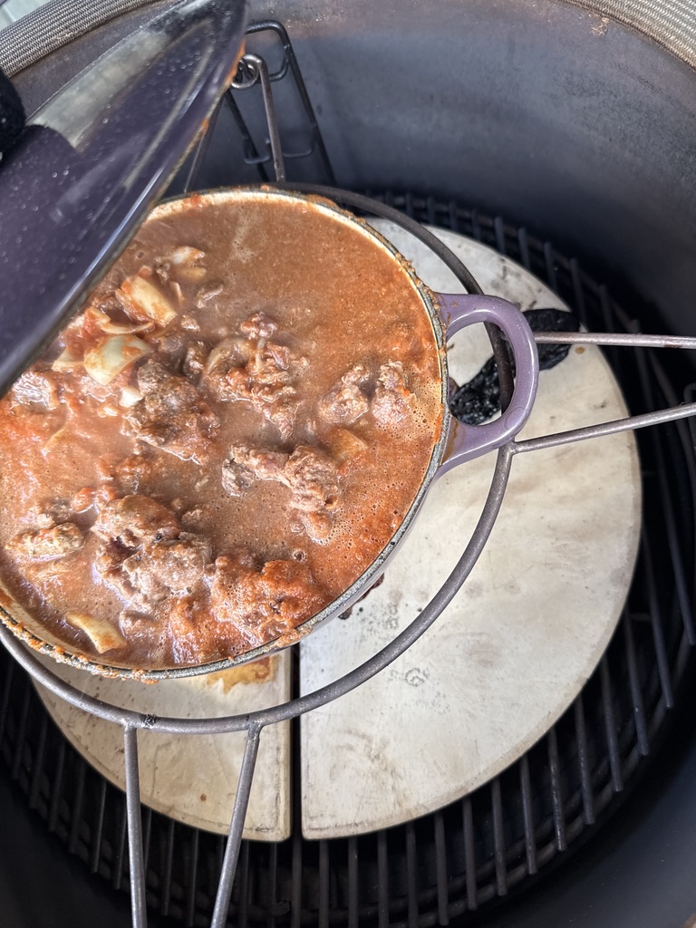 Beef pieces breaking down in simmering birria broth inside a Kamado BBQ