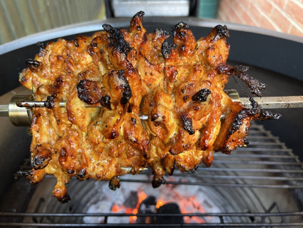 Chicken shawarma stacked on a rotisserie spit over glowing charcoal in a Kamado grill