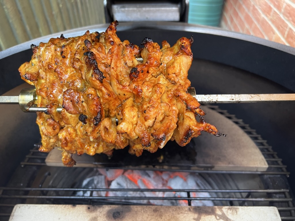 Close view of chicken shawarma on a rotisserie spit inside a Kamado grill