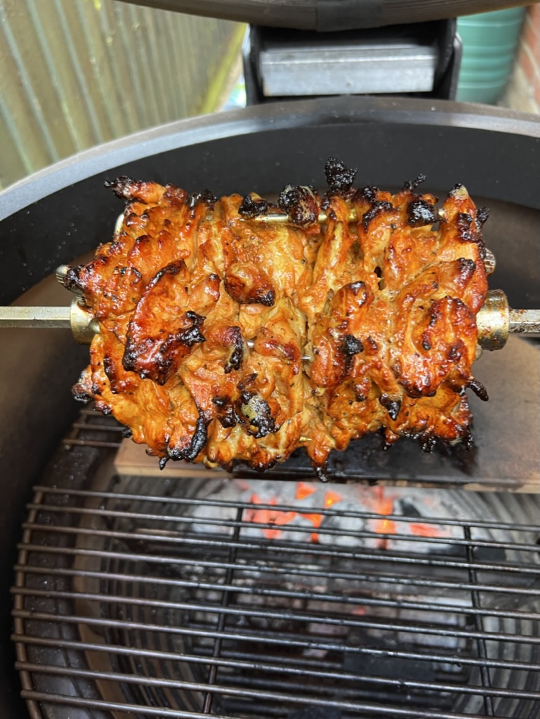 Front view of browned chicken shawarma on a rotisserie spit in a Kamado grill
